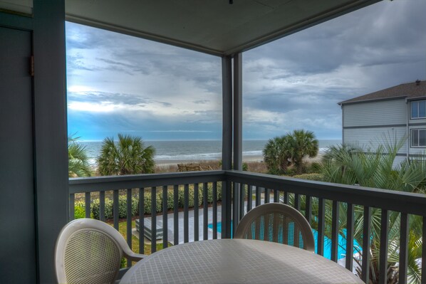 A covered balcony with a view of the beach and ocean.
