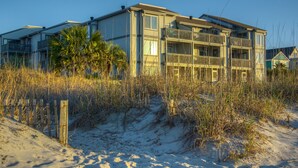 Una propiedad frente a la playa con un edificio de dos pisos, una playa arenosa al frente y una cerca de madera.