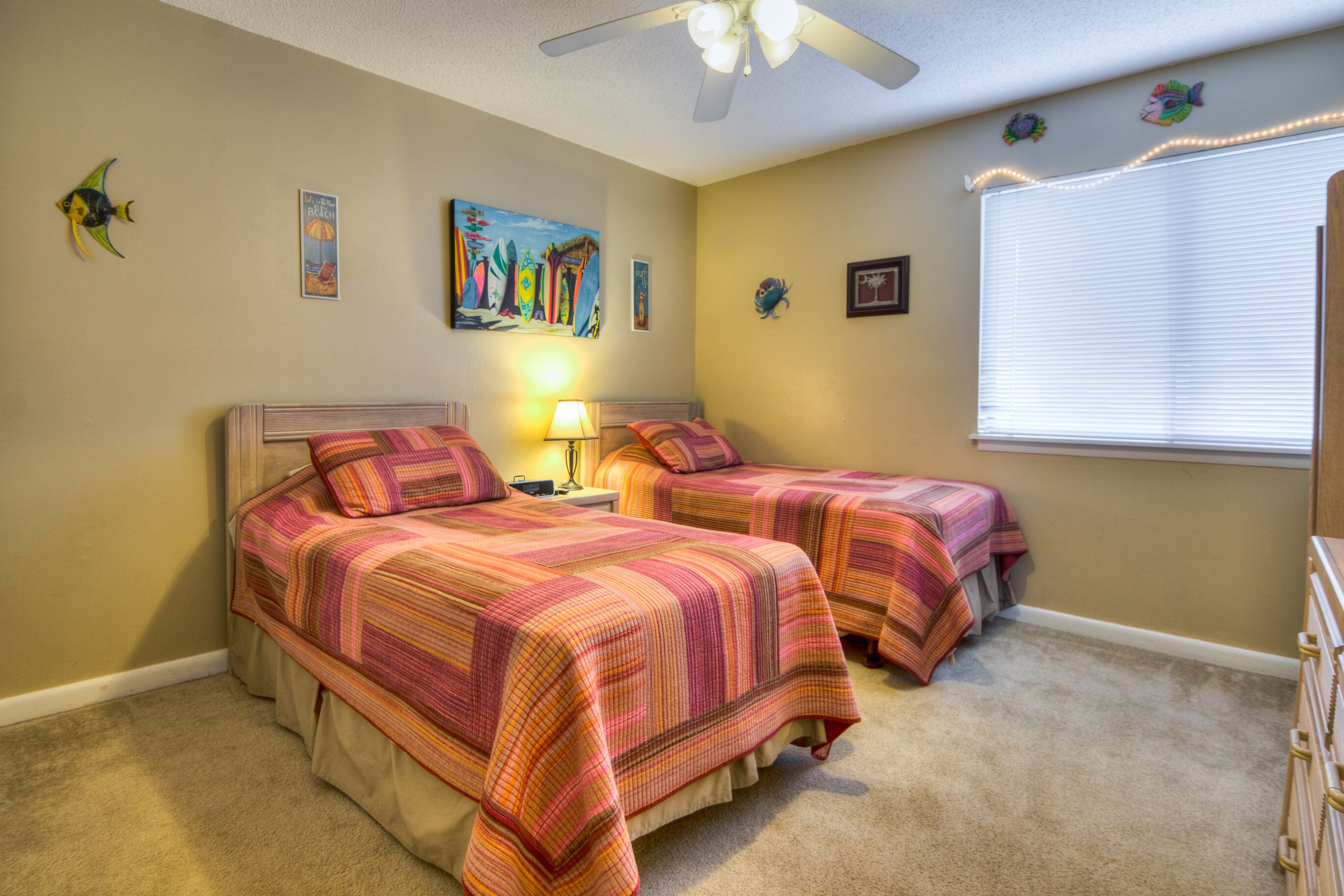 A bedroom with two beds, a ceiling fan, and a window with blinds.
