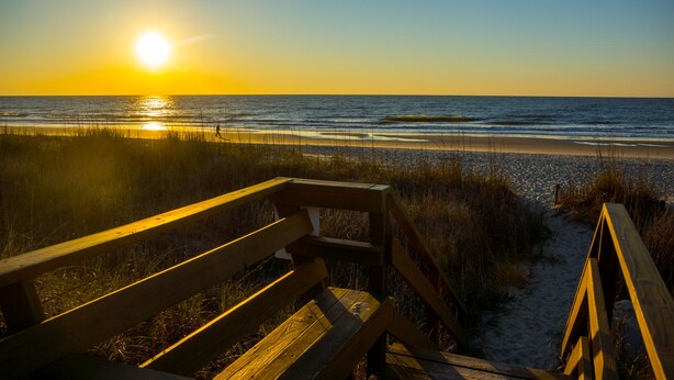 Un banco de madera con vista a una playa al atardecer.