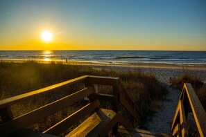 A wooden bench overlooking a beach at sunset.