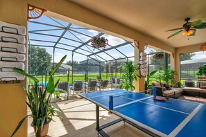 Un patio couvert comprenant une table de ping-pong, des sièges et des plantes en pot.