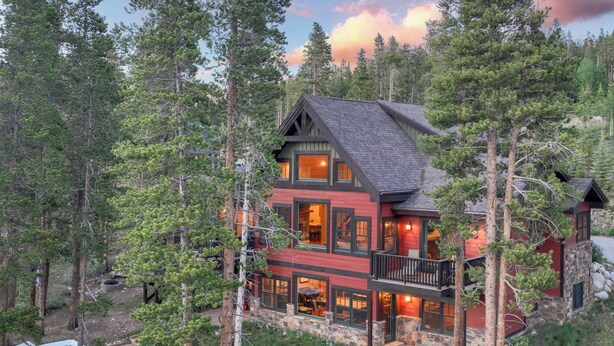 A two-story cabin with a stone foundation, large windows, and a balcony.