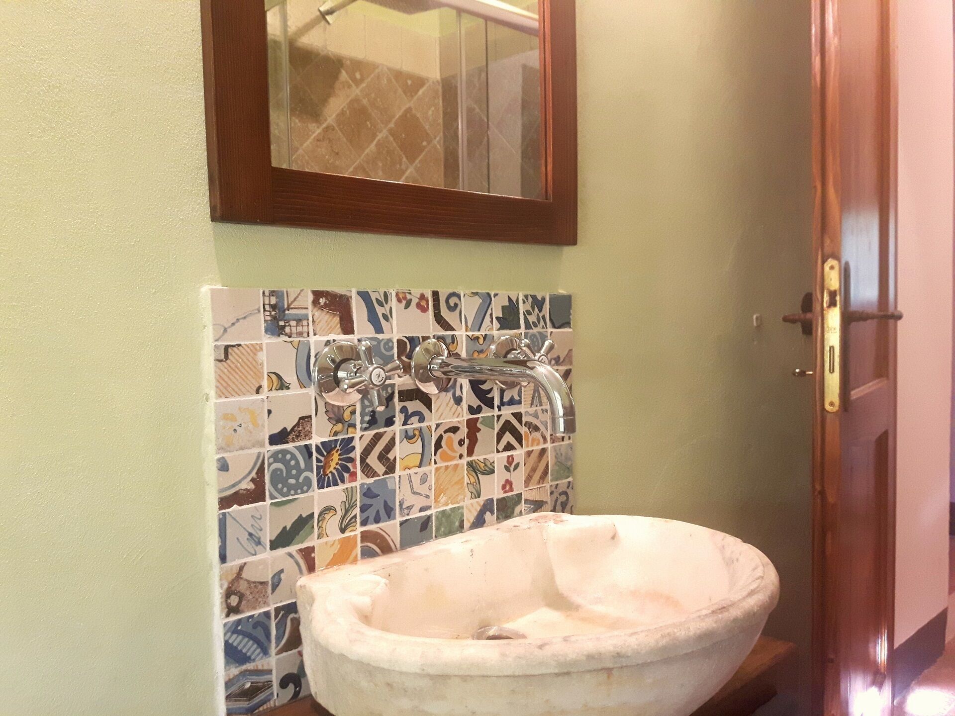 Un baño con pared de mosaicos, un lavabo de cerámica blanca y una puerta de madera.