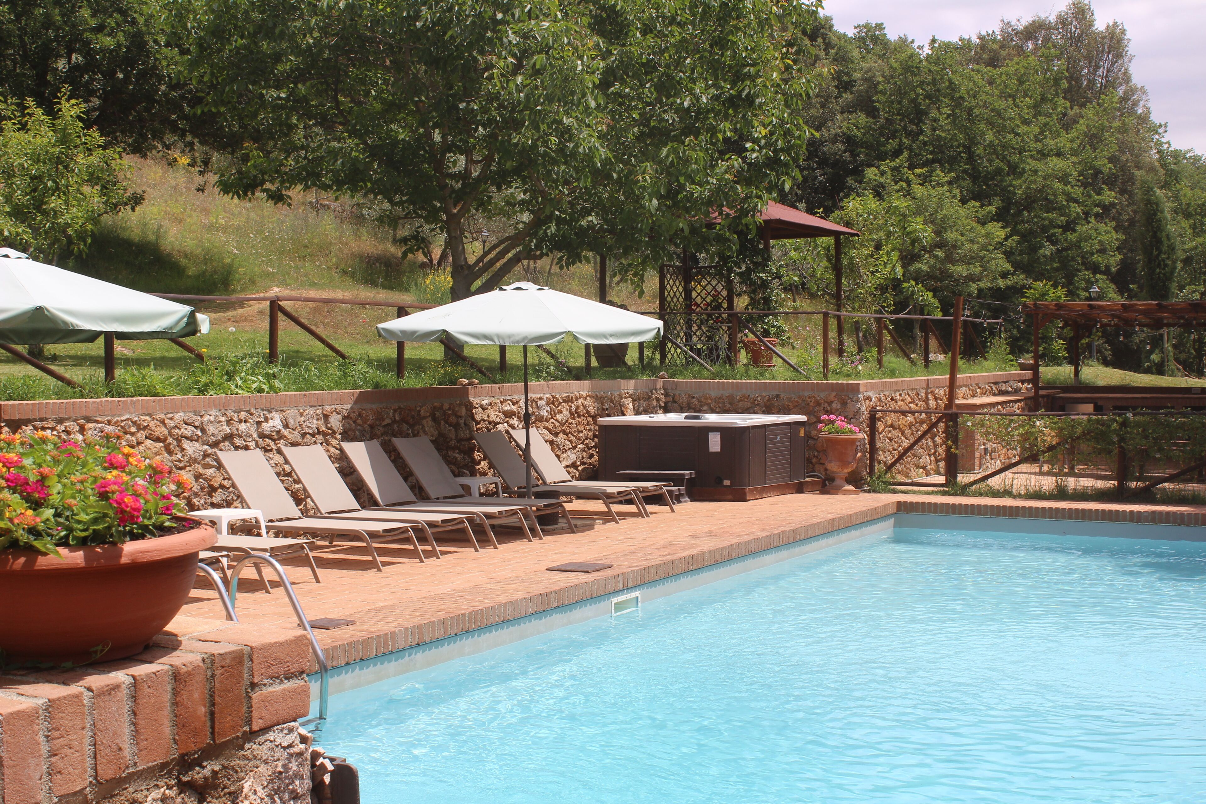 A swimming pool with lounge chairs and umbrellas, surrounded by a stone wall and greenery.