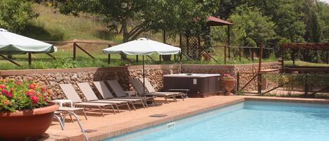 A swimming pool with lounge chairs and umbrellas, surrounded by a stone wall and greenery.