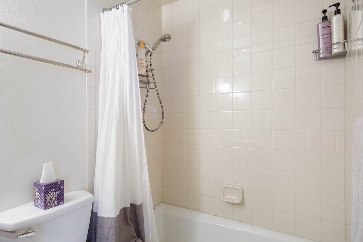 Un baño con ducha, inodoro y estante con artículos de aseo.