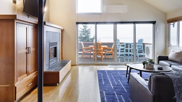 A modern living room with a fireplace, a large sliding glass door leading to a balcony, and a flat-screen TV mounted on the wall. - Stunning, Modern Alki Beach View Home (Seattle)