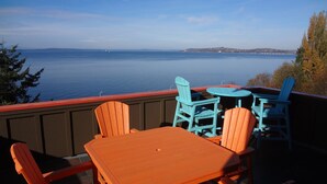 A patio with wooden furniture overlooking a body of water. - Stunning, Modern Alki Beach View Home (Seattle)