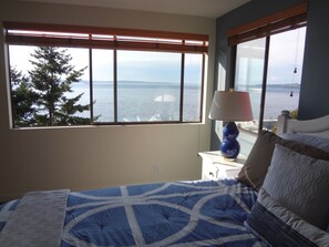 Enjoy a serene view of the water from this cozy bedroom with a large window, a comfortable bed, and stylish bedside lamps.