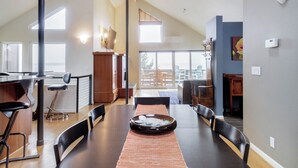 A dining area with a long table, chairs, a central decorative bowl, and a view of the outdoors through large windows. - Stunning, Modern Alki Beach View Home (Seattle)