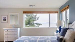 A bedroom with a bed, a dresser, a nightstand, a lamp, and a window with a view. - Stunning, Modern Alki Beach View Home (Seattle)