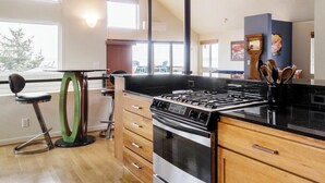 A modern kitchen with a gas stove, wooden cabinets, and a large window overlooking a deck. - Stunning, Modern Alki Beach View Home (Seattle)
