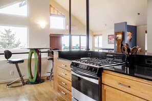 A modern kitchen with a gas stove, wooden cabinets, and a large window overlooking a deck.