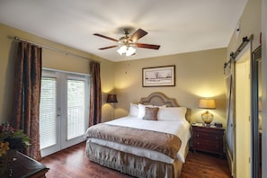 Une chambre d’hôtel avec un lit, un ventilateur de plafond, une table de chevet, une lampe et un tableau encadré au mur.