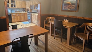 A dining area with wooden tables and chairs, a chandelier, and a kitchen visible through an archway. - Fishing, Hunting, Hiking, And Lots Of Family Fun!! Direct View of Escudilla Mtn (Nutrioso)