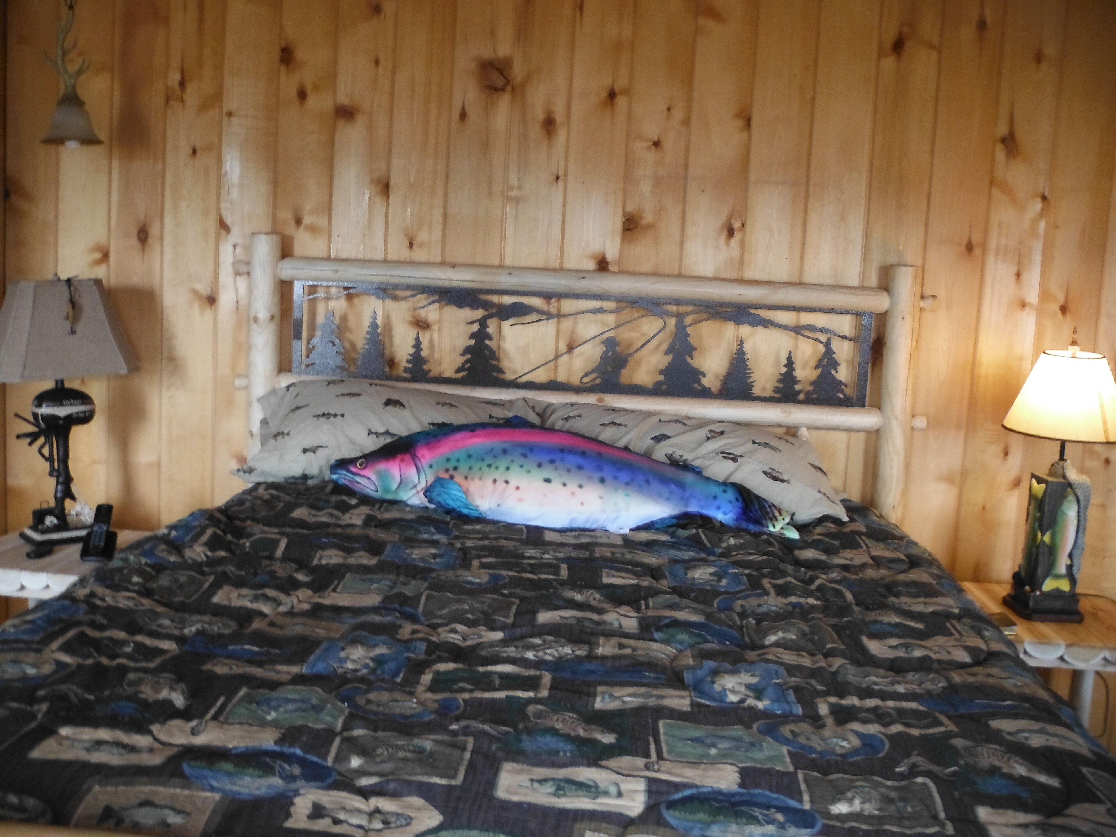 A bed with a fish-shaped pillow, a patterned bedspread, and a wooden headboard.
