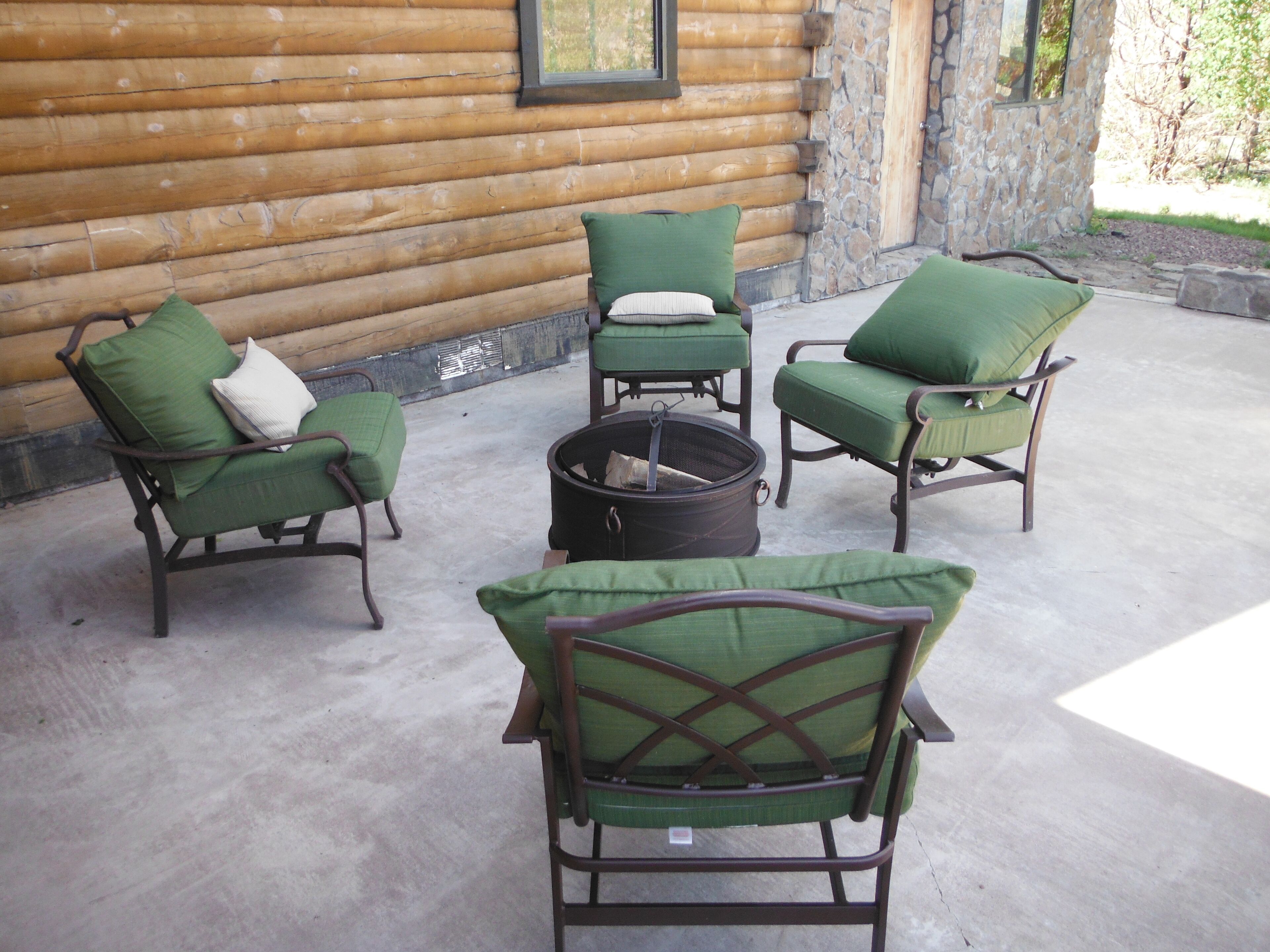 A log cabin with a stone exterior, a fire pit, and four green cushioned chairs arranged around it.
