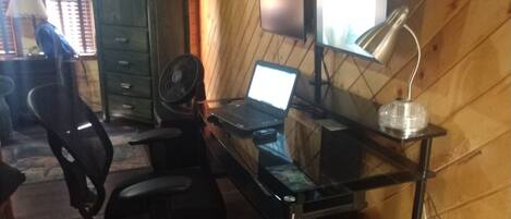 Een kamer met houten inrichting, een bureau met een laptop, een stoel, een ventilator en een kast.