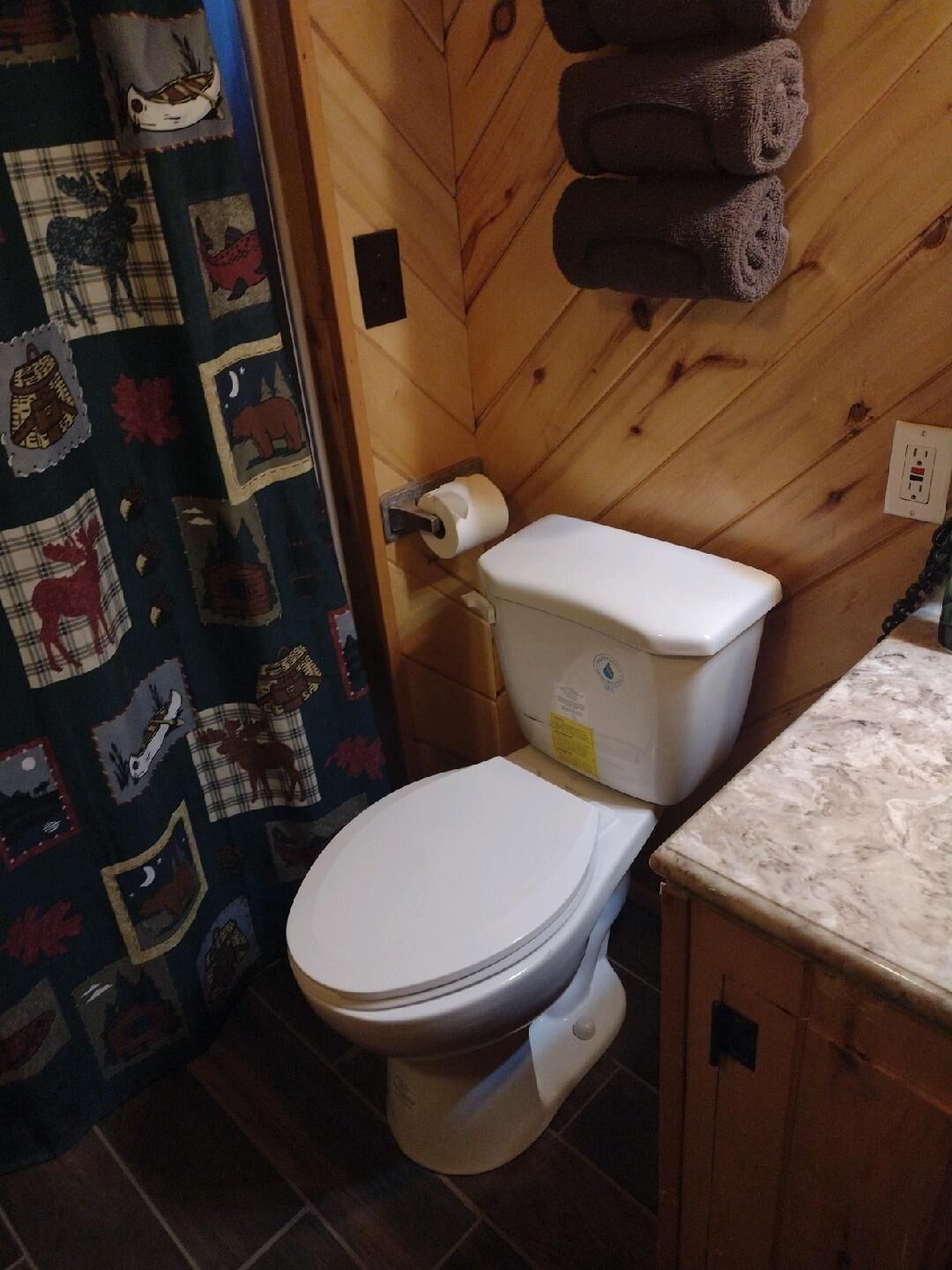Ein Badezimmer mit Holzwand, Toilette, Toilettenpapierrolle und Handtuchhalter mit Handtüchern.