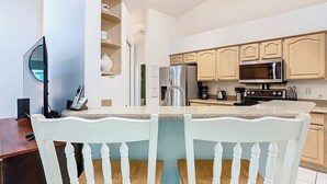 A modern kitchen with white cabinetry, a built-in microwave, and a refrigerator. There are two white chairs with wooden seats and backs. - ALWAYS FREE POOL HEAT - 2 KINGS, Games room! 5 smart TV’s - S/Steel appliances (Kissimmee)