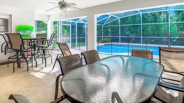 A spacious patio with a glass-top table and chairs, a ceiling fan, and a view of a swimming pool. - ALWAYS FREE POOL HEAT - 2 KINGS, Games room! 5 smart TV’s - S/Steel appliances (Kissimmee)
