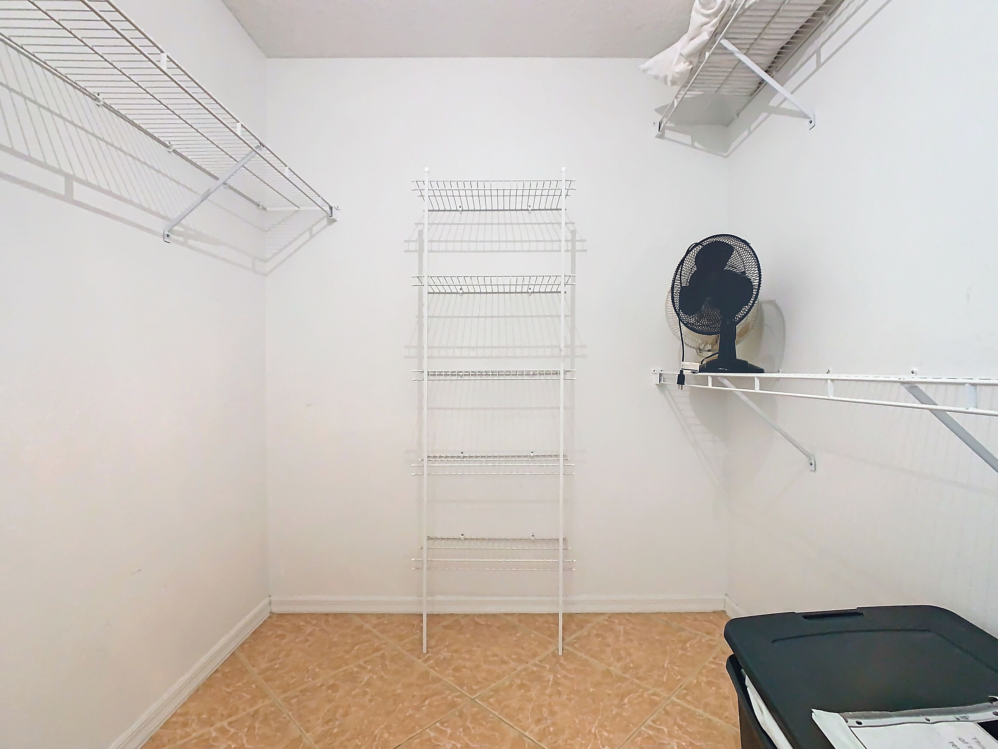 A room with a metal drying rack, a black fan, and a tiled floor.