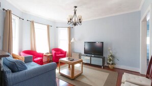 Un salon avec un canapé bleu, un fauteuil rouge et un téléviseur posé sur un meuble.