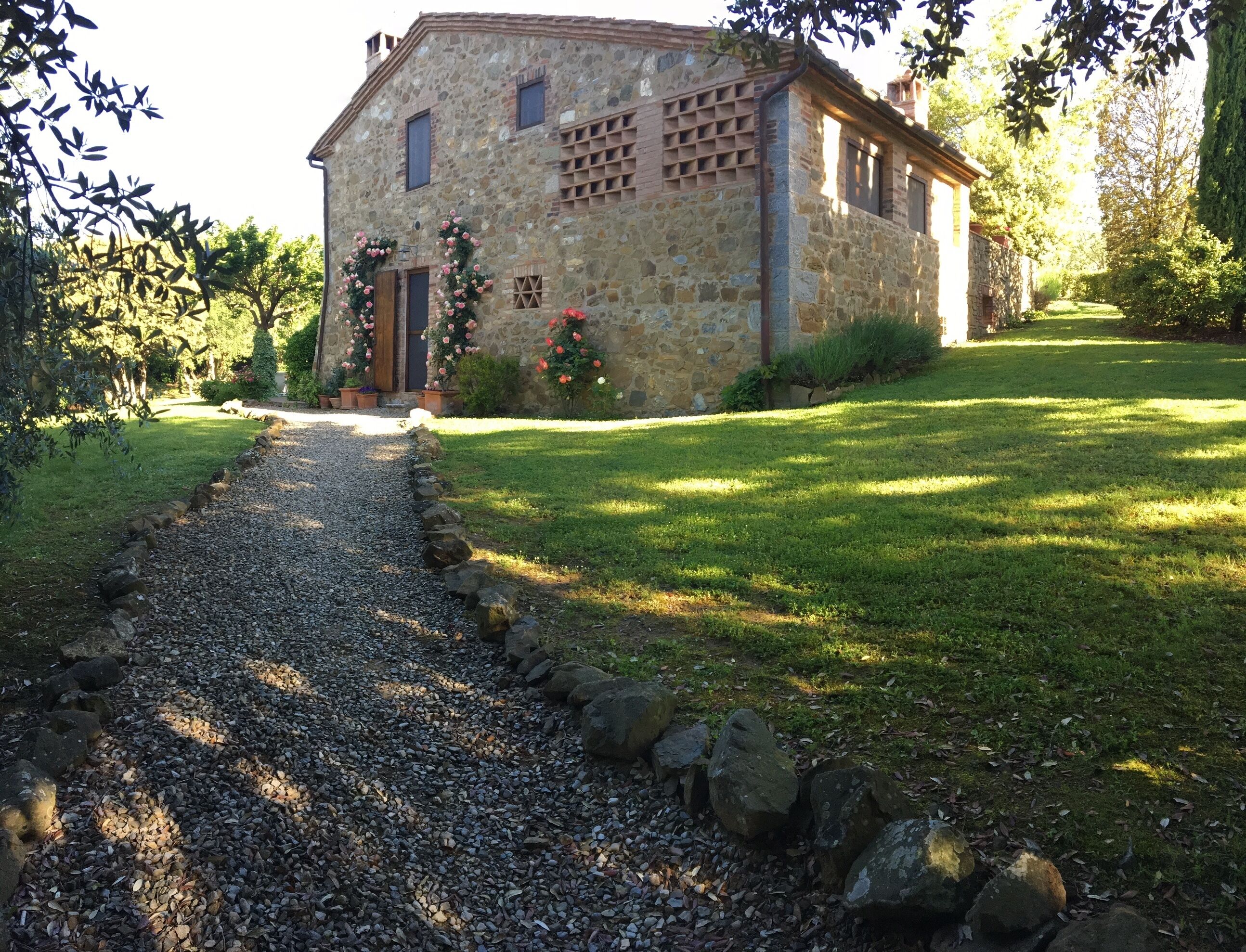 Un edificio de piedra con un sendero de grava que conduce a la entrada, rodeado de follaje y un césped cuidado.