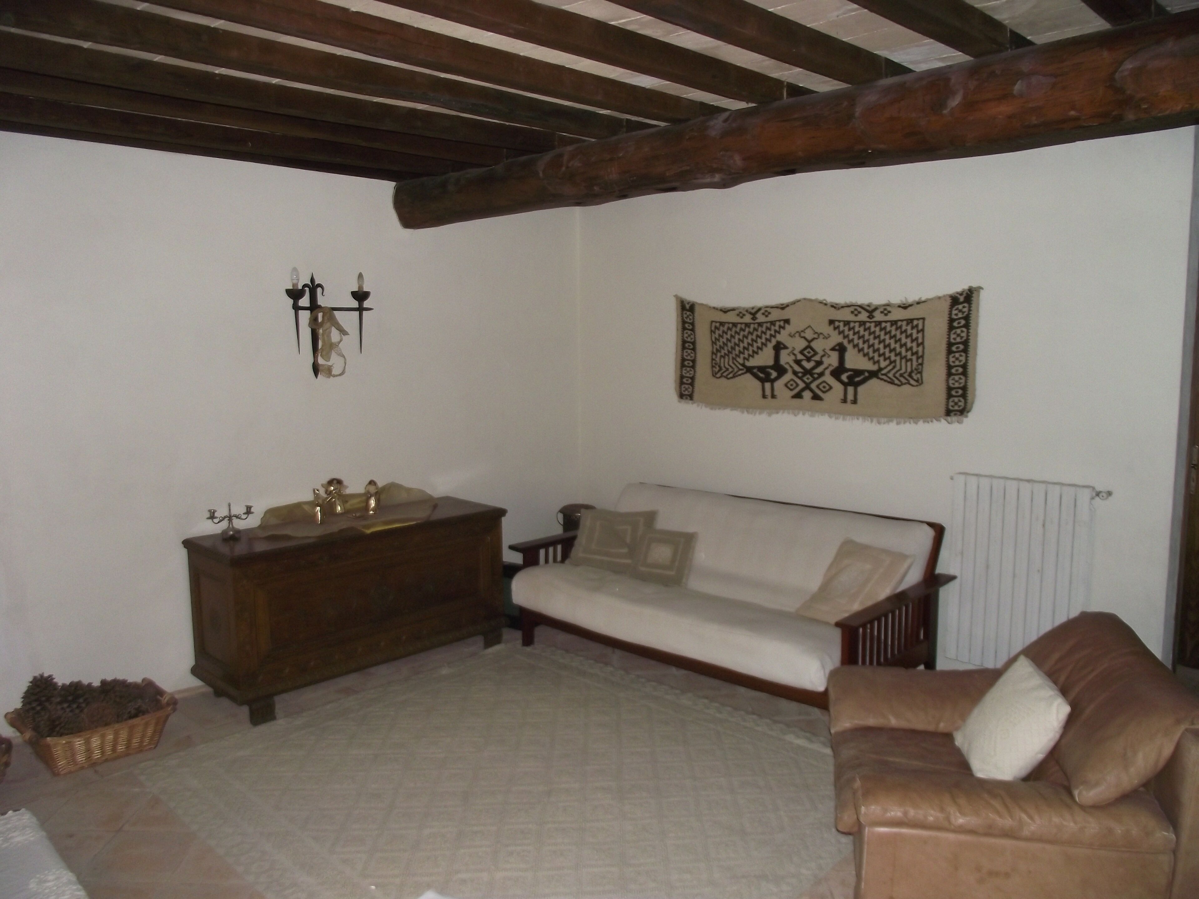 A room with a wooden ceiling, a sofa, a brown leather chair, a wooden dresser, and a tapestry on the wall.