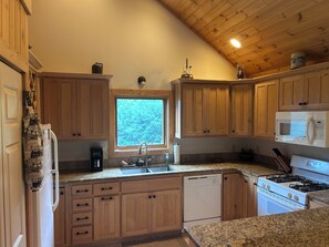 A kitchen with wooden cabinets, a window, a sink, a dishwasher, a stove, and a microwave.