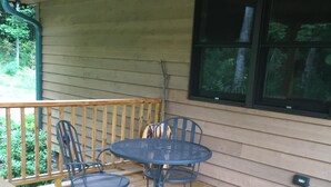 A wooden deck with a metal table and chairs, a wooden bench, and a window with a view of trees. - Blue Ridge Mountains (West Jefferson)