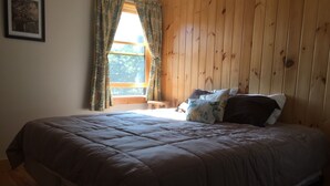 A bedroom with a large bed, wooden walls, a window with curtains, and a small bench. - Blue Ridge Mountains (West Jefferson)