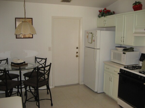 A compact kitchen with a refrigerator, microwave, stove, and a dining table with chairs. - Luxury 4 Bedroom Villa, 5 Minutes From Disney, South Facing Pool And Spa (Kissimmee)
