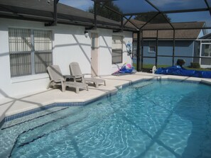 A swimming pool with clear water, surrounded by a covered area with lounge chairs and a door. - Luxury 4 Bedroom Villa, 5 Minutes From Disney, South Facing Pool And Spa (Kissimmee)