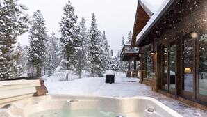 A snow-covered outdoor area with a hot tub, wooden deck, and a building with large windows. - Last Nickel Lodge: Private Home on Golf Course, Hot Tub, Pool Table, Foosball (Breckenridge)