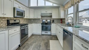 Une cuisine moderne avec des meubles blancs, une cuisinière en acier inoxydable et une grande fenêtre qui laisse entrer la lumière naturelle.