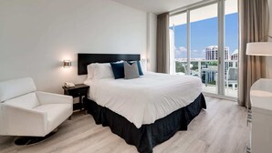 A modern hotel room with a large bed, a white armchair, a bedside table with a lamp, and a city view through large windows. - City&Ocean View Balcony. Pool & Hottub. Fast Wi-Fi (Miami)