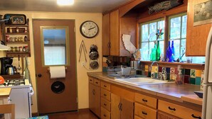 A kitchen with wooden cabinets, a sink, and a window with colorful tiles. - Find your vacation here, at Merrynook Cabin (Pinehurst)