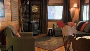 A cozy living room with a fireplace, wooden floors, and a mix of seating arrangements including a sofa and chairs. - Find your vacation here, at Merrynook Cabin (Pinehurst)
