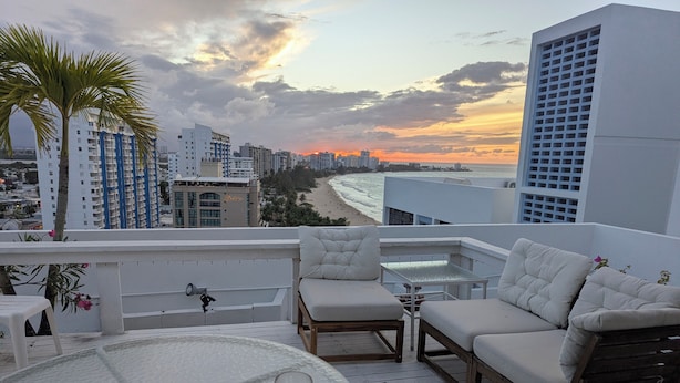 A rooftop terrace with a view of the beach and cityscape, furnished with a table and chairs. - Rooftop, private garden penthouse, 2 beach view Bedrooms, free parking, WIFI (Isla Verde, Carolina)