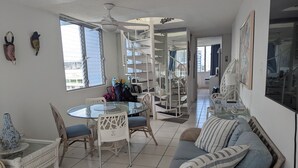 A spacious living area with a round glass table, wicker furniture, a sofa with striped pillows, and a spiral staircase. - Rooftop, private garden penthouse, 2 beach view Bedrooms, free parking, WIFI (Isla Verde, Carolina)