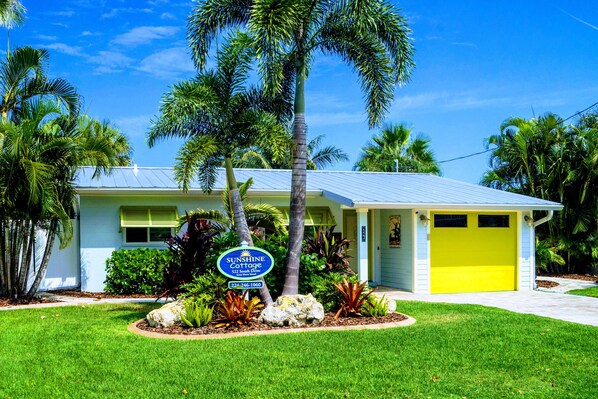 A two-story house with a bright yellow garage door, surrounded by lush greenery and palm trees. - Boater's Dream!  1/2 Block from Beach- Private Boat Dock & 30' Pool. (Anna Maria)