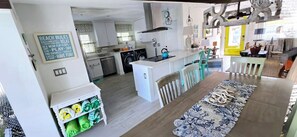 A modern kitchen with white cabinets, a central island, and a dining area with a patterned rug. - Boater's Dream!  1/2 Block from Beach- Private Boat Dock & 30' Pool. (Anna Maria)