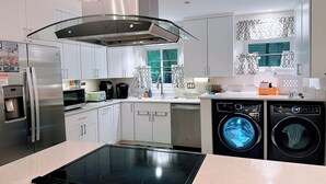 Une cuisine moderne avec des meubles blancs, un réfrigérateur en acier inoxydable, un four encastré, un lave-vaisselle et un lave-linge.
