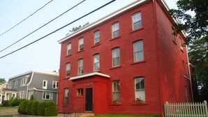A red two-story building with a front entrance, a small porch, and a white picket fence.