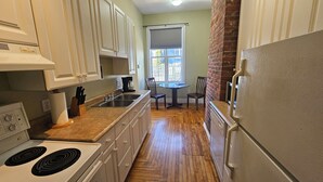 A narrow kitchen with white cabinets, a stove, a sink, and a refrigerator.
