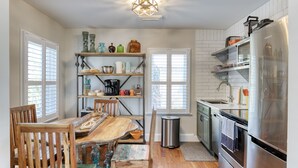 A kitchen with a wooden table, chairs, shelves with kitchenware, a stainless steel refrigerator, and a trash can. - Upstairs so Sunny and Bright 2 Blocks to the Beach (Folly Beach)