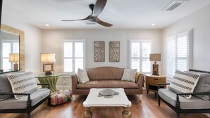 A spacious living room with a brown sofa, two armchairs, a glass coffee table, and a ceiling fan. - Upstairs so Sunny and Bright 2 Blocks to the Beach (Folly Beach)