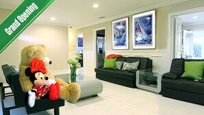 Een ruime woonkamer met een groot knuffelbeer, een bank en een salontafel. Er hangen kunstwerken in lijsten aan de muur en een deur die naar een andere kamer leidt.